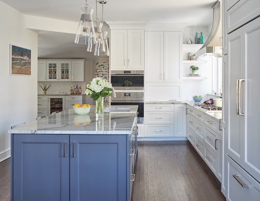 Modern white kitchen with navy blue island, quartz countertops, and stainless steel appliances by Design First Builders
